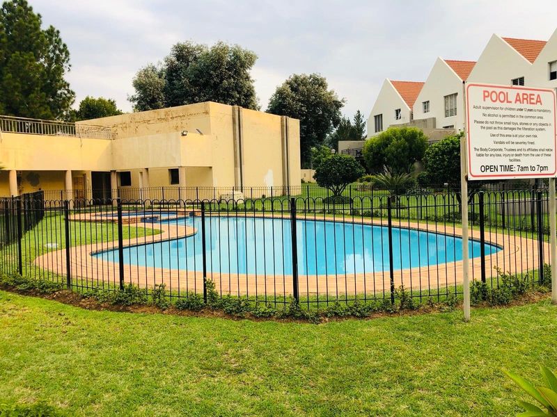 Communal swimming pool area featuring a fenced pool, paved surround, and landscaped lawn within an apartment complex.