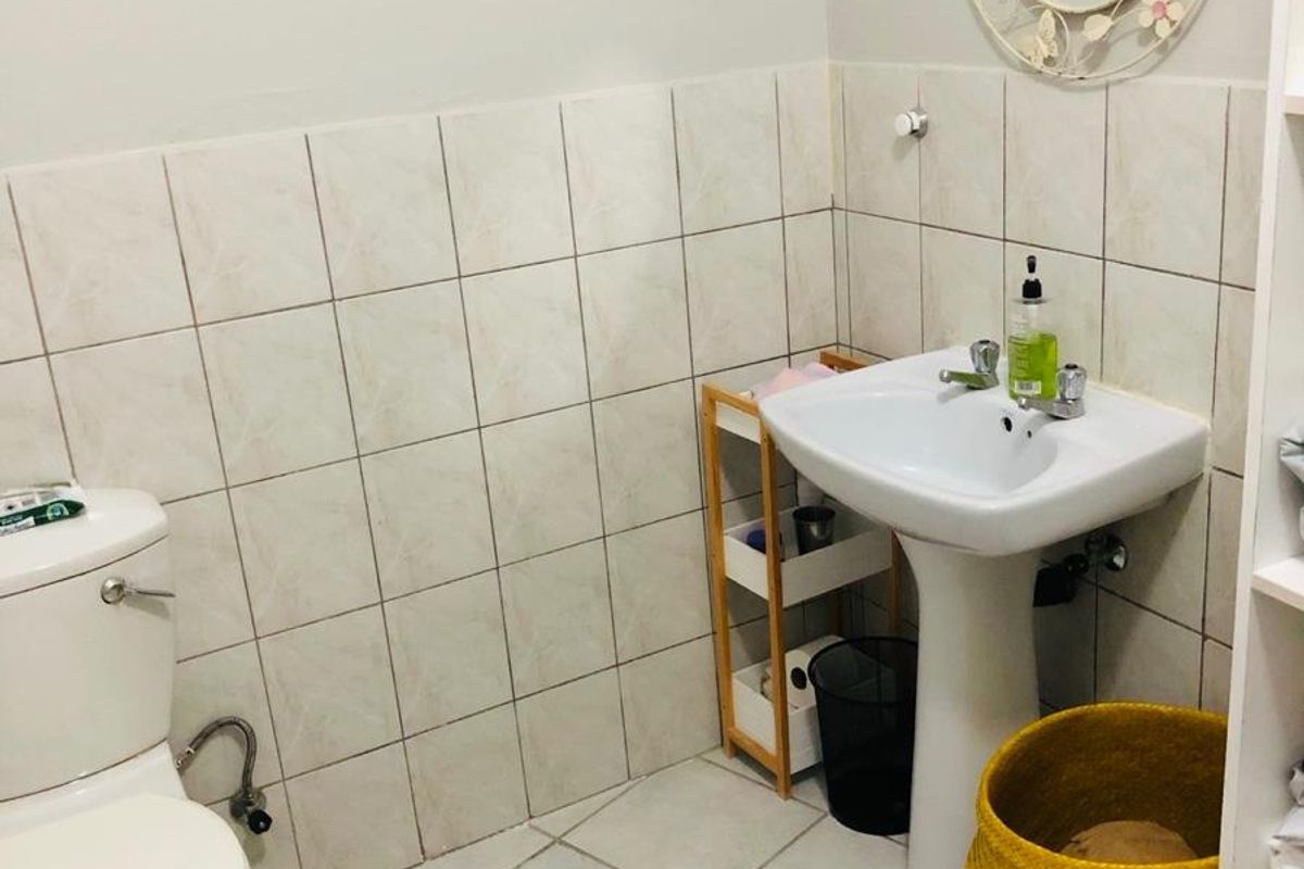 A functional bathroom featuring a pedestal sink, standard toilet, and neutral wall and floor tiling.