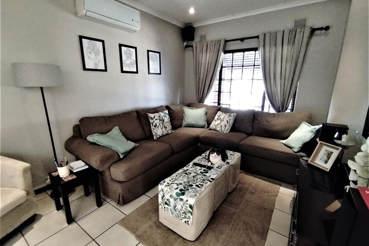 A comfortable living room featuring tiled flooring, a wall-mounted air conditioning unit, and a window with curtain treatments.