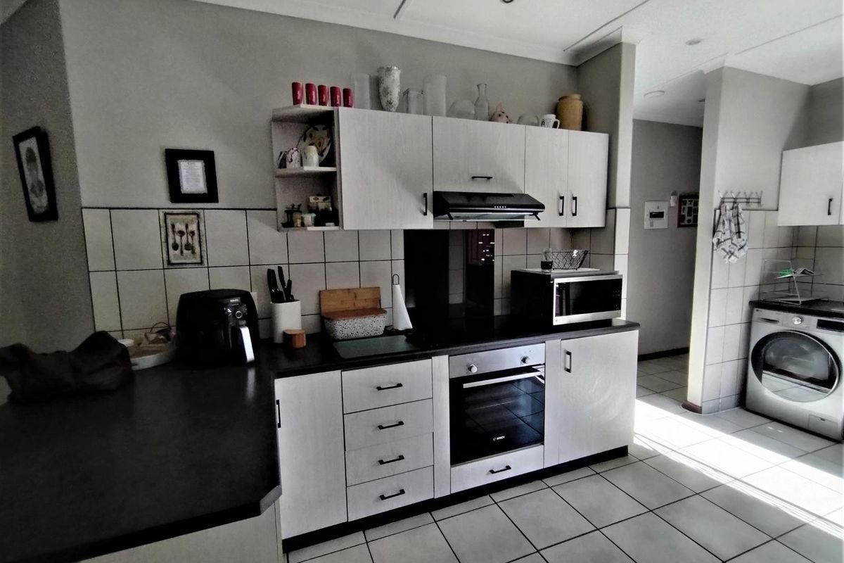 Functional kitchen featuring light-toned cabinetry, dark countertops, built-in oven, extractor fan, and integrated laundry space with tiled flooring throughout.