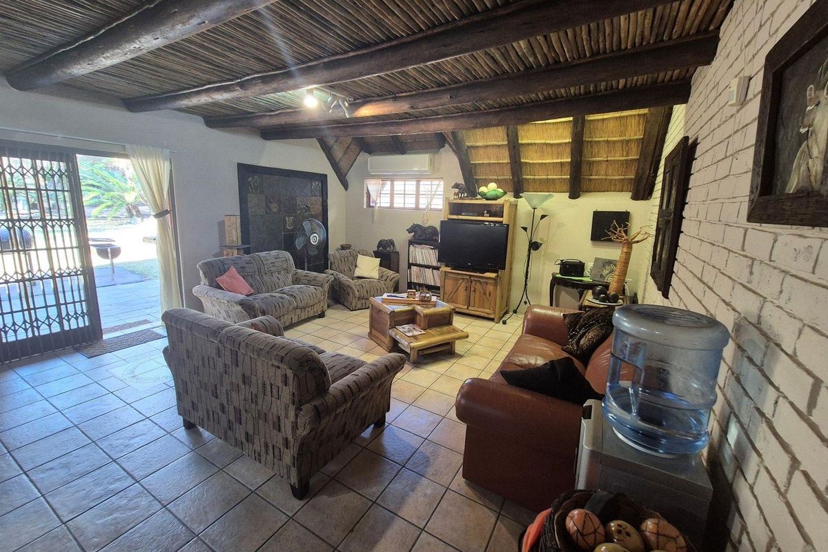 A rustic living room featuring a traditional thatched roof with exposed timber beams, tiled flooring, and sliding glass doors leading to an outdoor patio area.