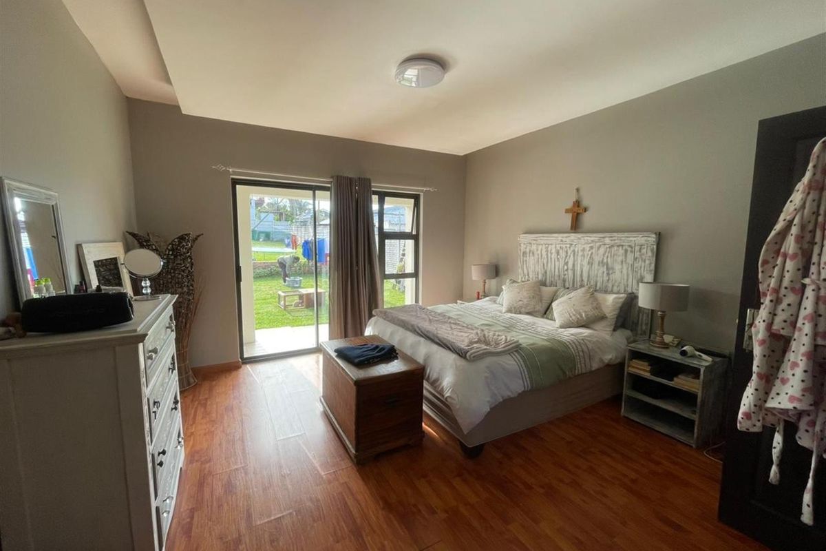 A well-maintained bedroom featuring wood-look flooring, a tray ceiling, and sliding glass doors providing direct access to the rear garden.