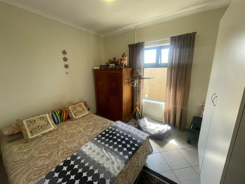 A functional bedroom featuring tiled flooring, a built-in cupboard, and natural light through an aluminium-framed window.