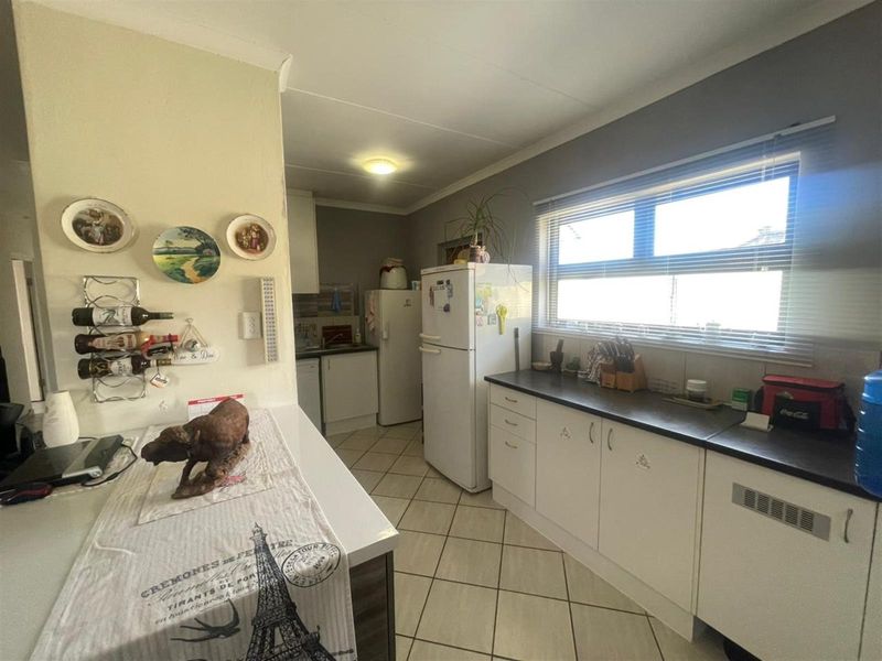 A functional kitchen featuring white cabinetry, dark laminate countertops, and tiled flooring, offering a practical layout with natural light from the side window.
