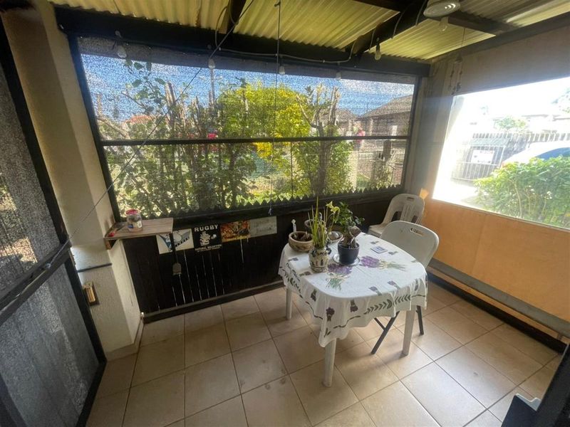 A covered patio area featuring tiled flooring, timber wall cladding, and shade netting, providing a functional outdoor space for relaxation.