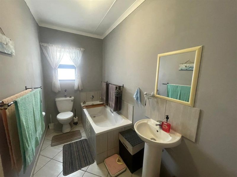 A functional bathroom featuring a pedestal basin, built-in bathtub, and toilet with neutral wall finishes and tiled flooring.