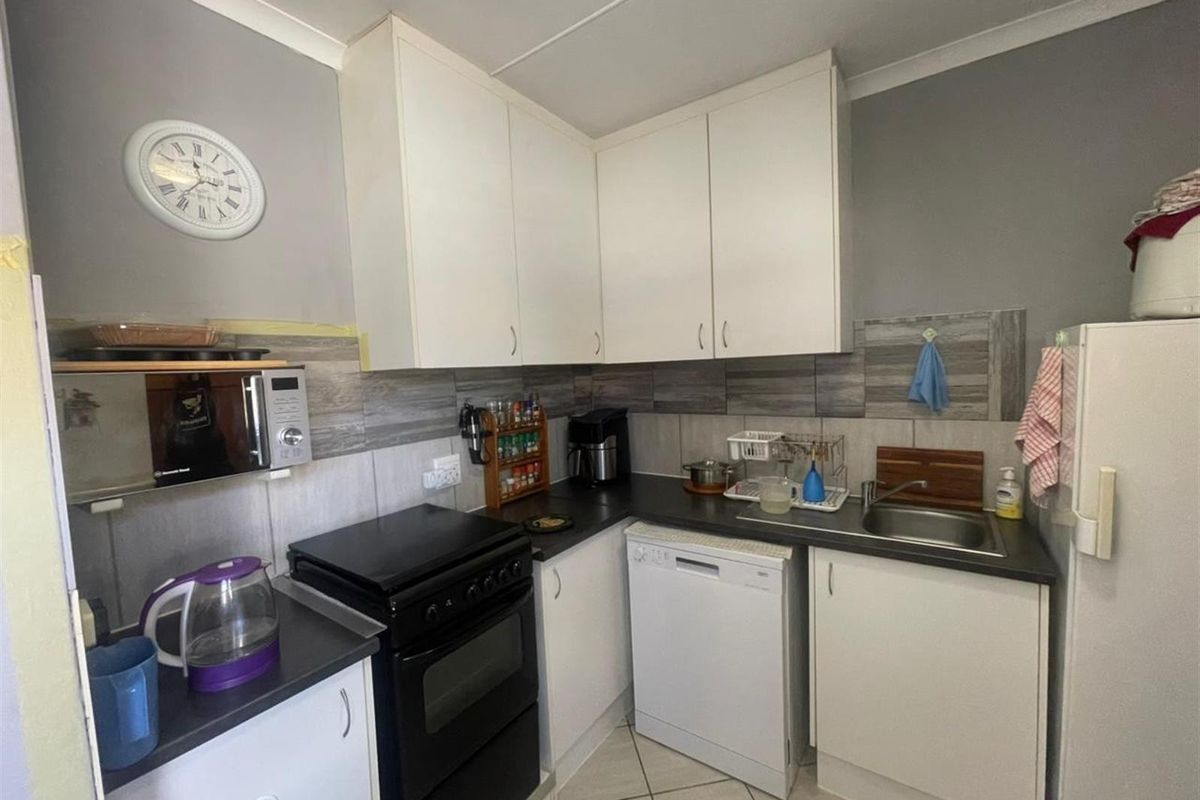 Compact kitchen featuring white cabinetry, dark countertops, tiled backsplash, and functional layout with space for essential appliances.