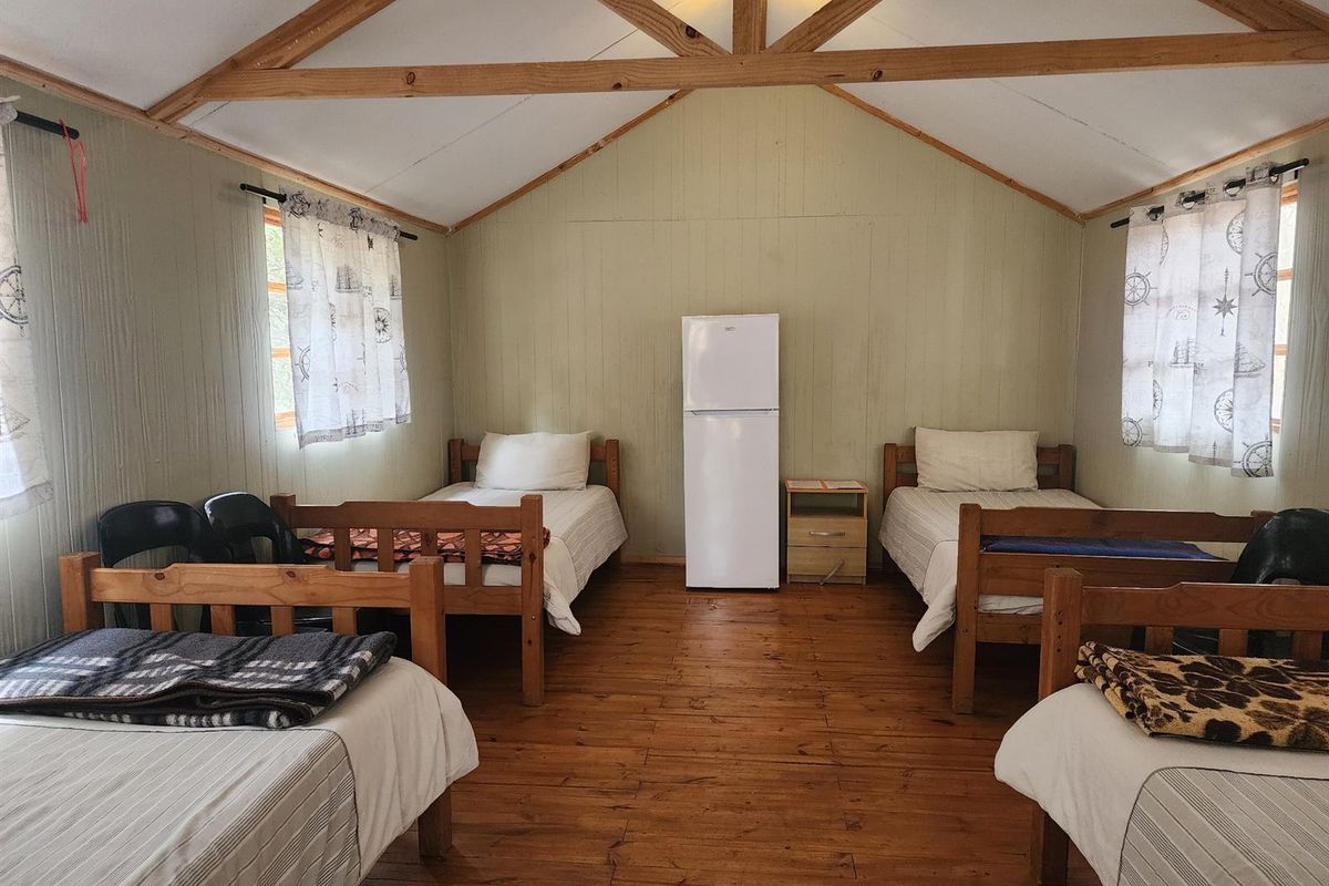 A rustic bedroom featuring exposed timber roof trusses, timber wall paneling, and timber flooring, providing a simple and functional accommodation space.