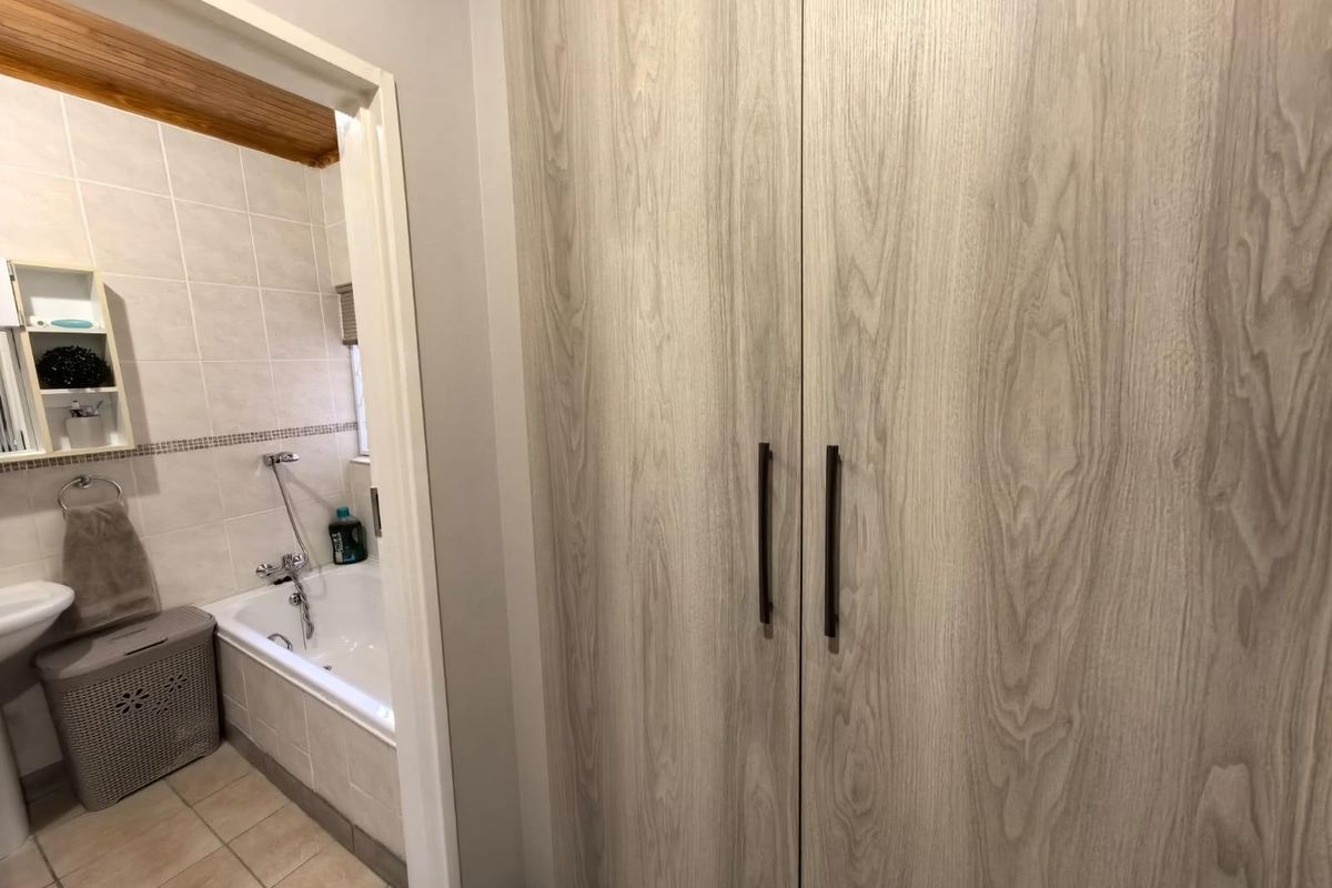 A view from a hallway into a bathroom featuring a built-in bathtub, tiled walls, and a large wood-grain finish built-in cupboard.