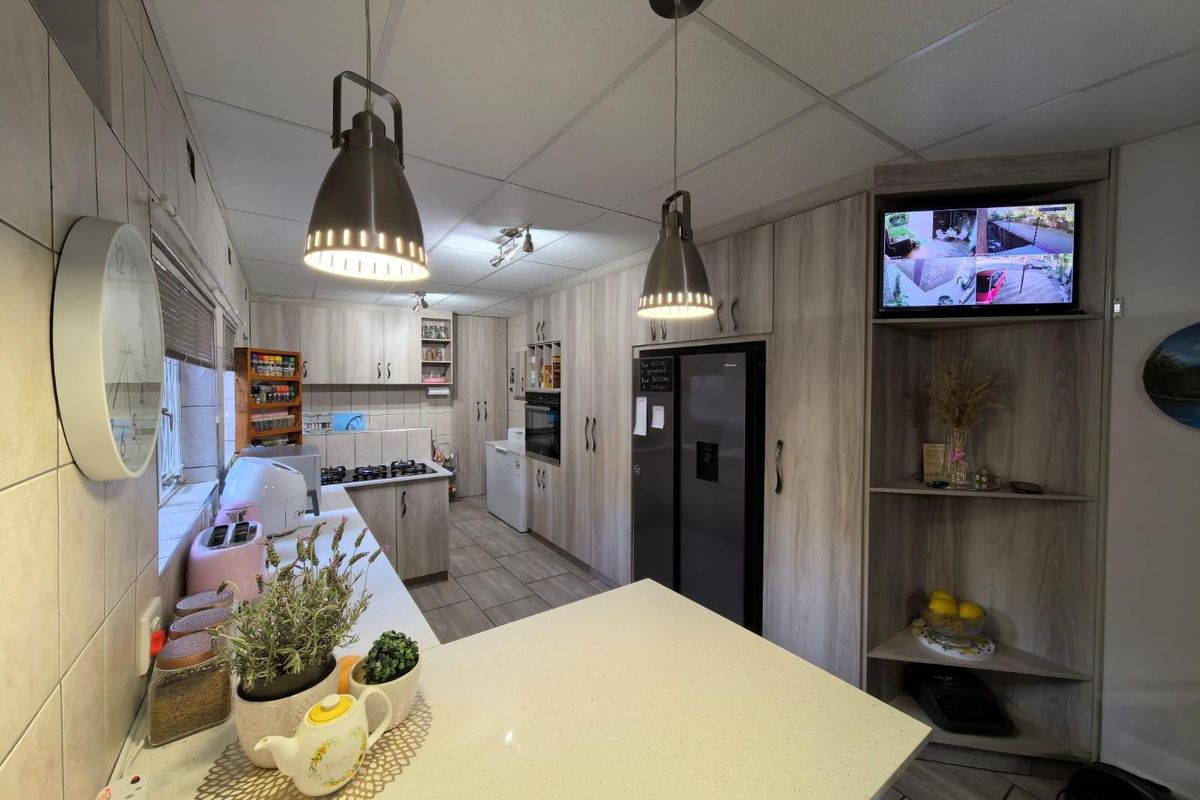A functional kitchen featuring light wood-grain cabinetry, stone-look countertops, built-in oven, gas hob, and modern pendant lighting.