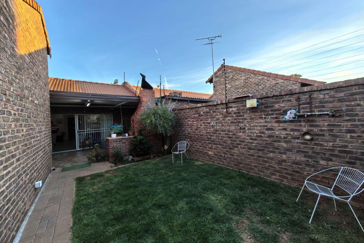 A private rear garden featuring a brick-paved walkway, a small lawn area, and a covered patio space attached to the townhouse structure.