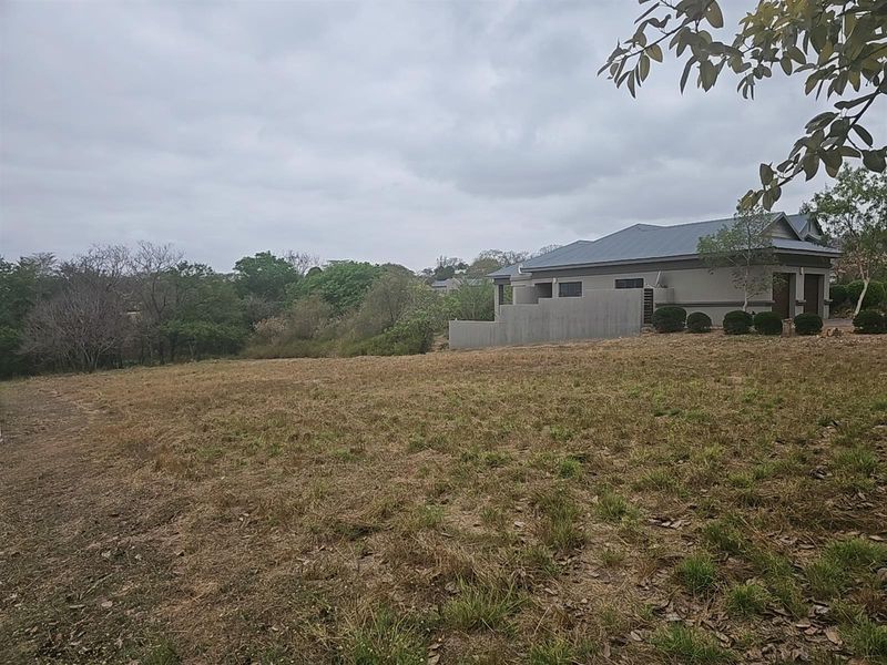 A view of a vacant residential plot with natural grass cover, adjacent to existing residential development.