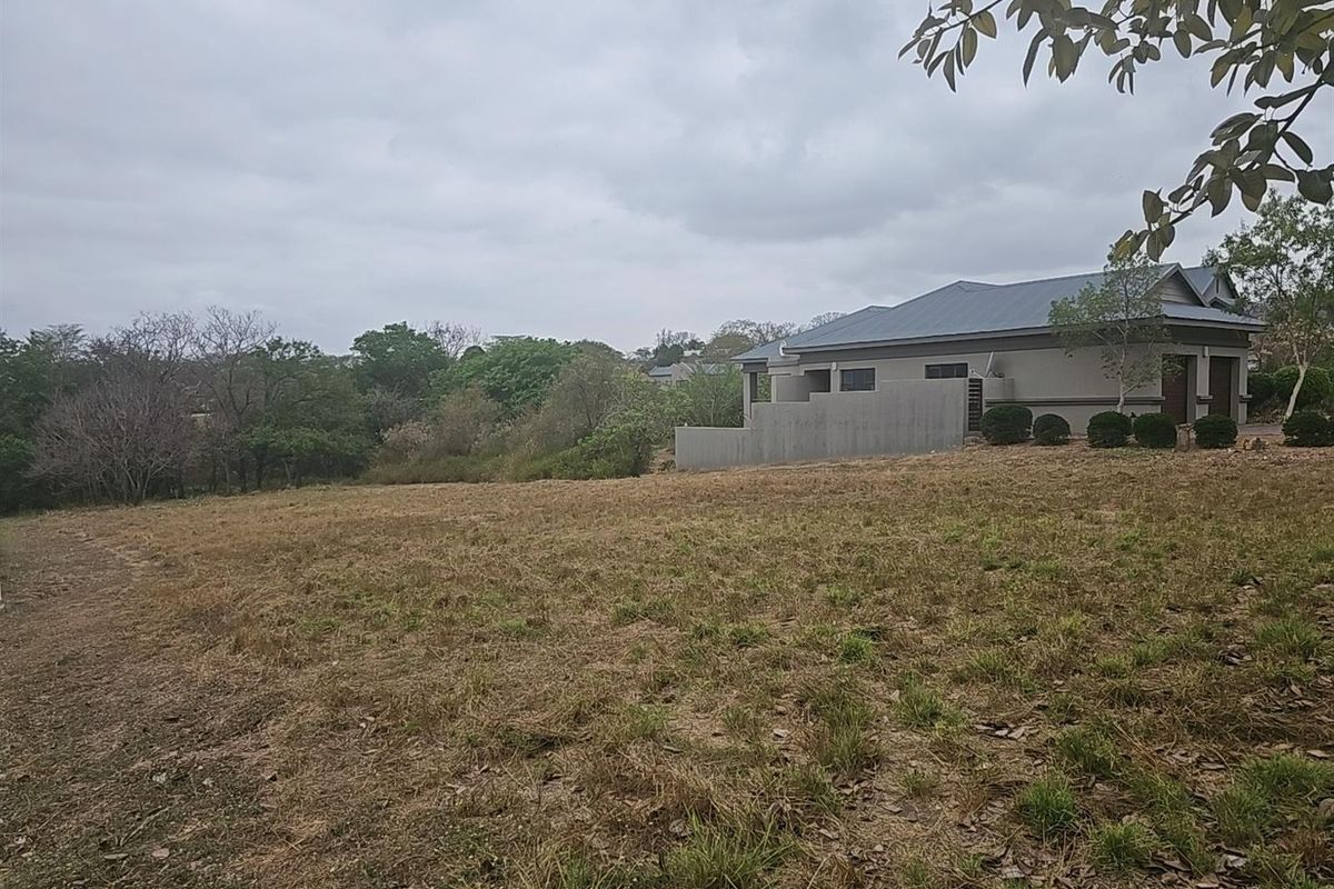 A view of a vacant residential plot with natural grass cover, adjacent to existing residential development.