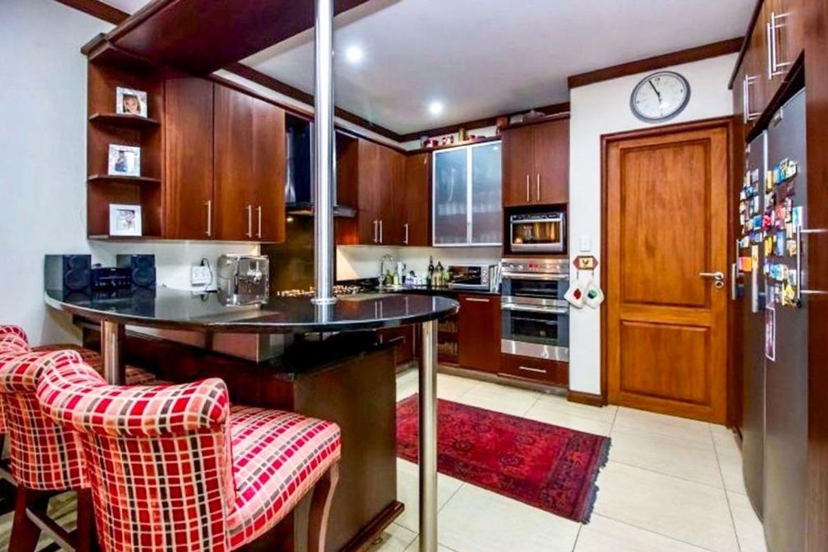 A functional kitchen featuring dark wood cabinetry, a breakfast bar with a metal support pillar, built-in oven, and tiled flooring.