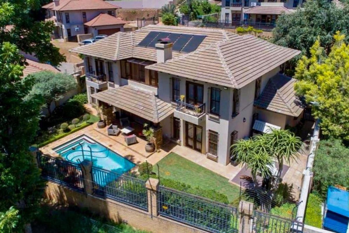 Aerial view of a multi-story residential property featuring a tiled roof with solar panels, a swimming pool, a patio area, and landscaped garden.