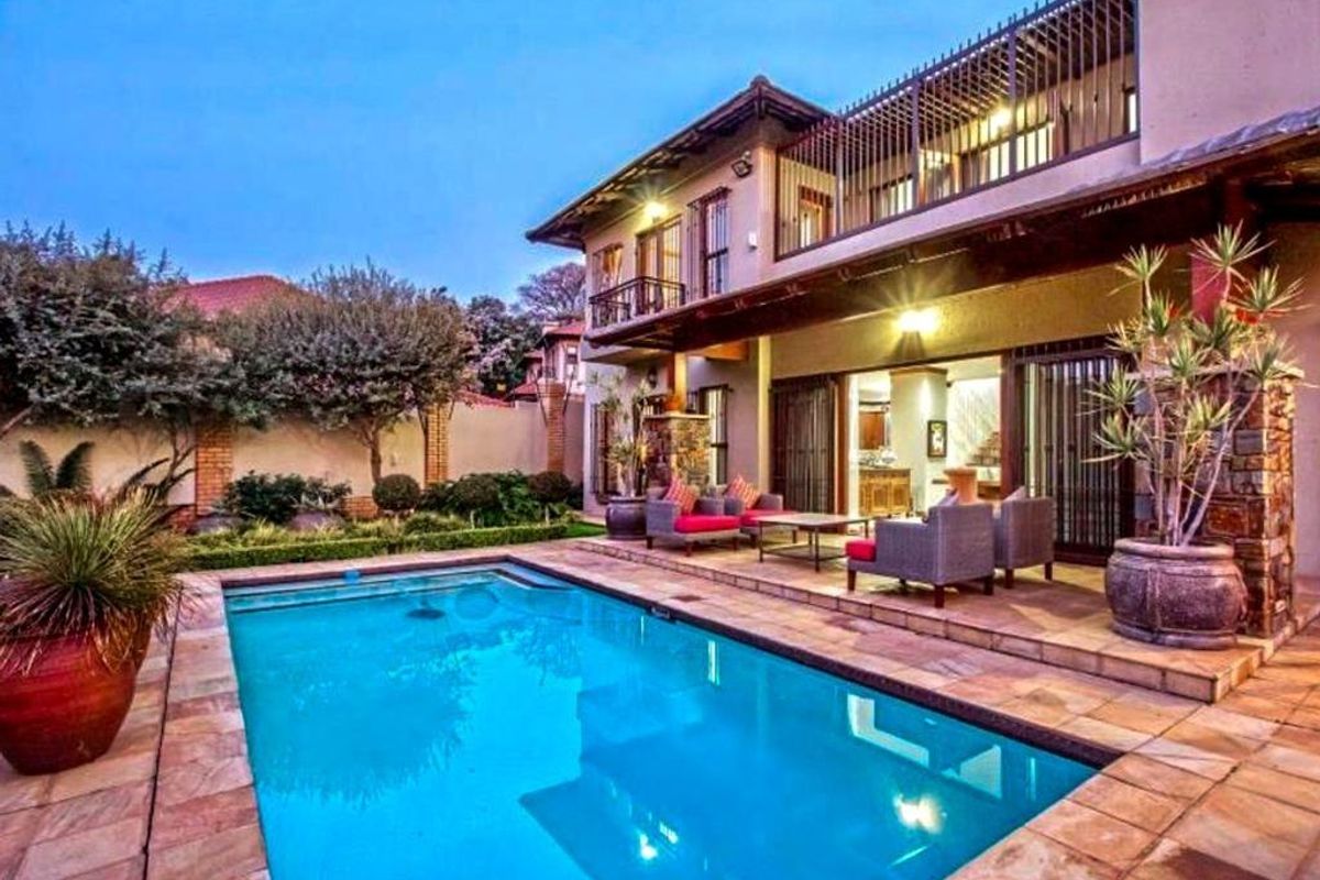 A well-maintained rear exterior featuring a swimming pool, paved patio area, and a two-story house facade with a balcony.