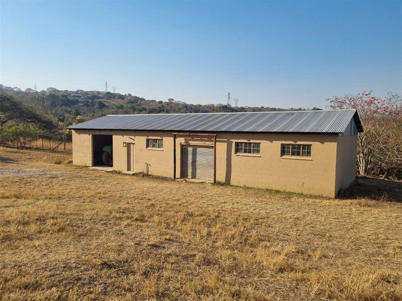 A detached utility building or workshop featuring concrete block construction, a corrugated metal roof, and a roller shutter door, situated on a rural plot.