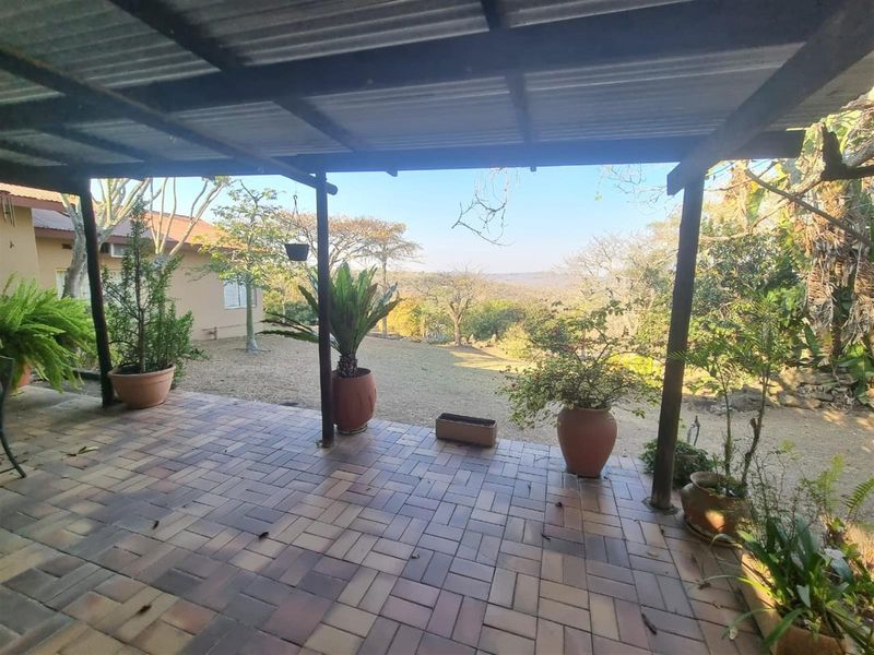 A covered outdoor patio featuring paved flooring and timber support posts, offering expansive views of the surrounding landscape and garden.