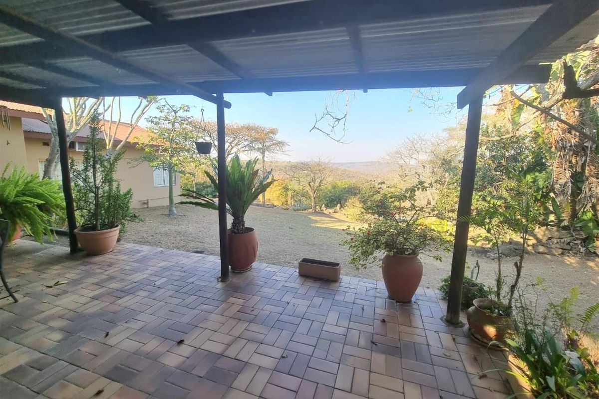 A covered outdoor patio featuring paved flooring and timber support posts, offering expansive views of the surrounding landscape and garden.