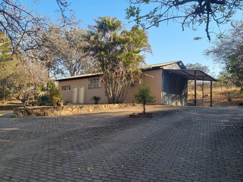 Exterior view of a property featuring a paved driveway, stone retaining wall, and a covered carport area with a metal roof.
