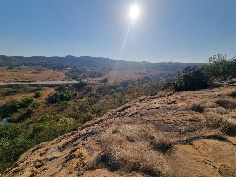 A scenic elevated view overlooking a natural landscape with rocky terrain and distant hills under a bright sun.