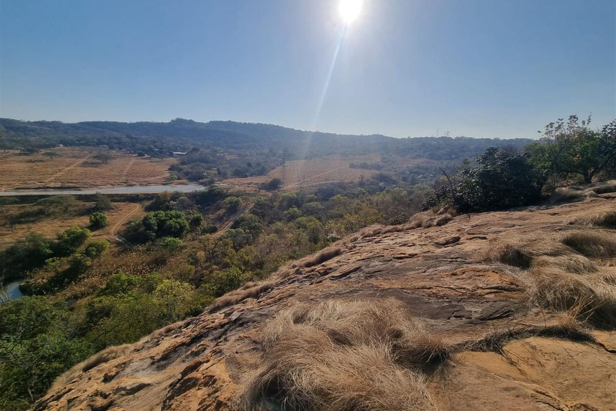 A scenic elevated view overlooking a natural landscape with rocky terrain and distant hills under a bright sun.