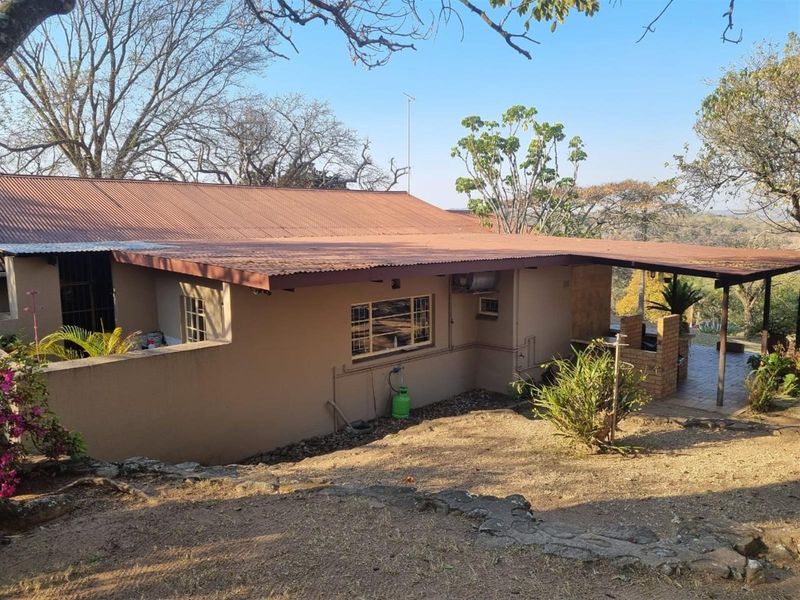 Rear view of the property featuring a covered patio area with a built-in brick braai and corrugated metal roofing.