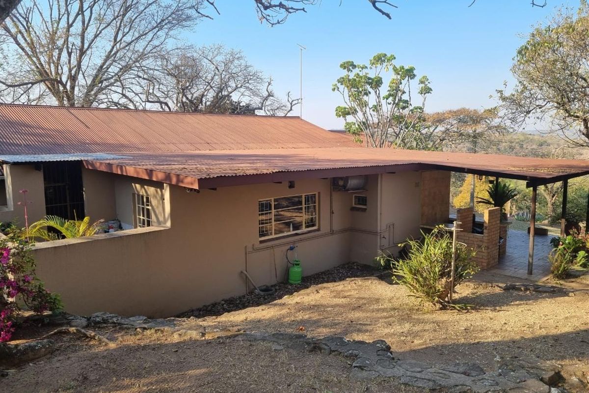 Rear view of the property featuring a covered patio area with a built-in brick braai and corrugated metal roofing.