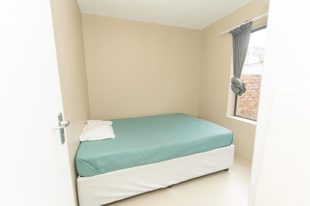 A compact bedroom featuring neutral wall tones, tiled flooring, and a window providing natural light.