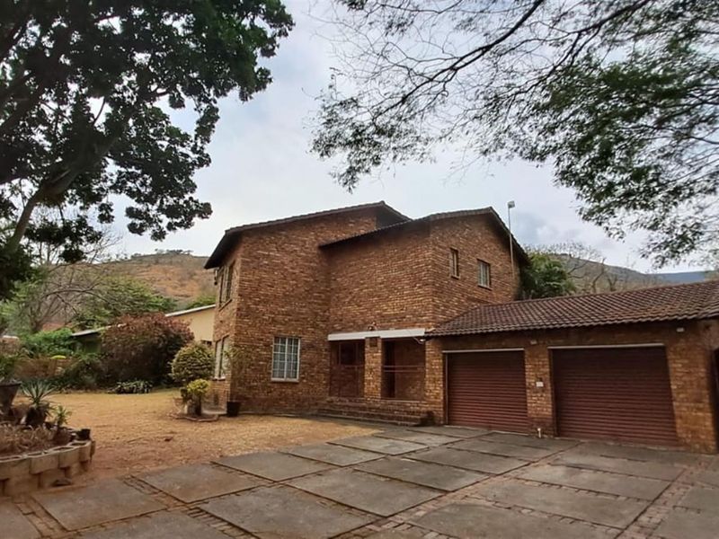 A double-story face-brick house featuring a double garage, paved driveway, and established garden setting with mountain views.