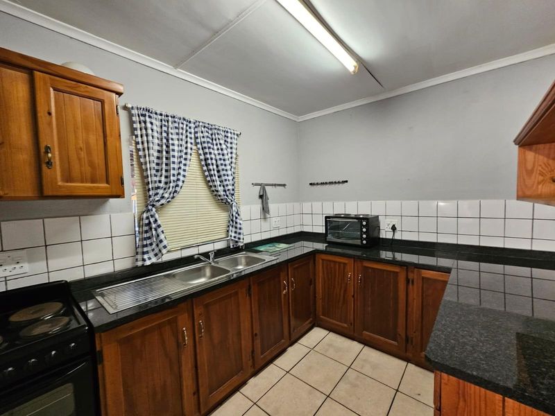 A functional kitchen featuring wooden cabinetry, granite countertops, a stainless steel double sink, and ceramic tiling throughout.