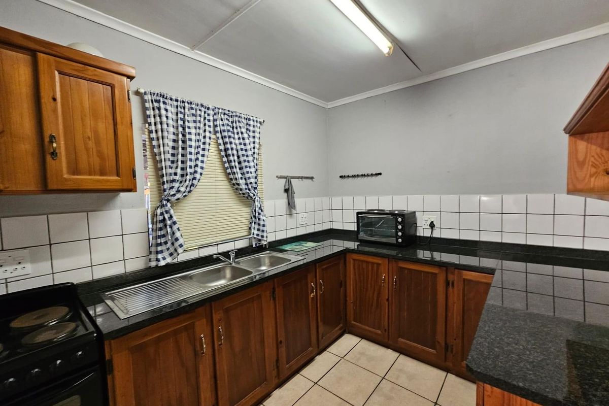 A functional kitchen featuring wooden cabinetry, granite countertops, a stainless steel double sink, and ceramic tiling throughout.