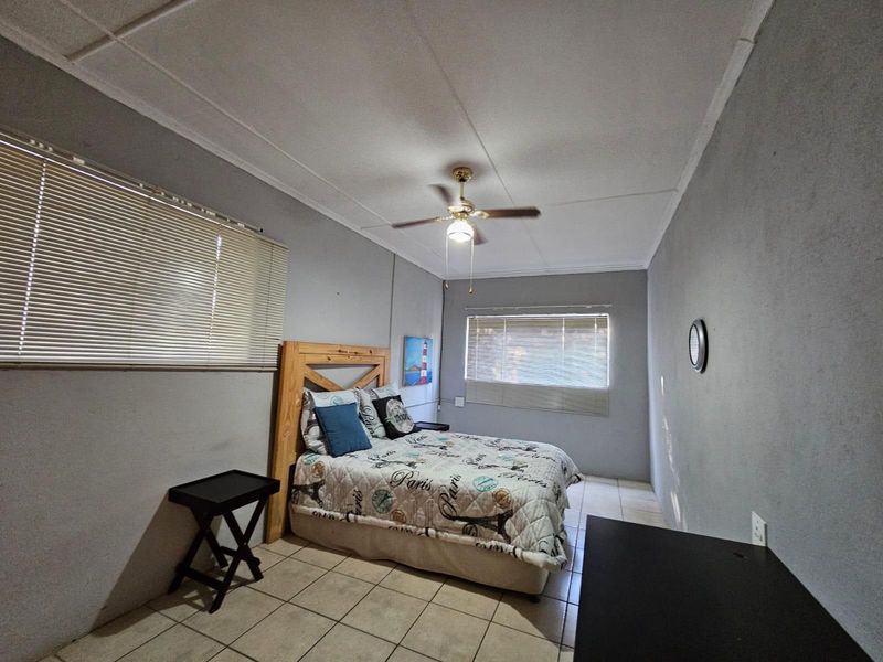 A functional bedroom featuring tiled flooring, a ceiling fan, and dual windows with venetian blinds, offering a neutral base for personalization.