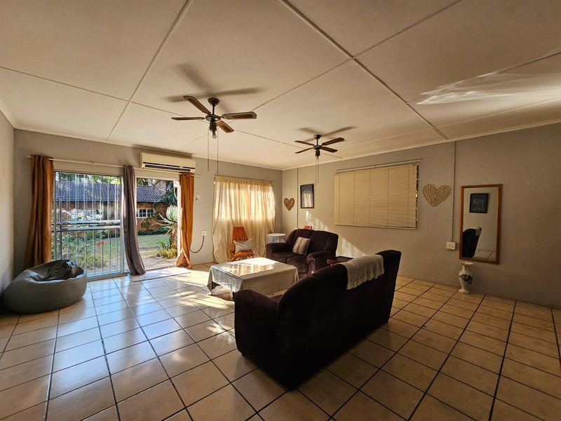Spacious living room featuring tiled flooring, dual ceiling fans, and direct access to the rear garden through a sliding glass door.