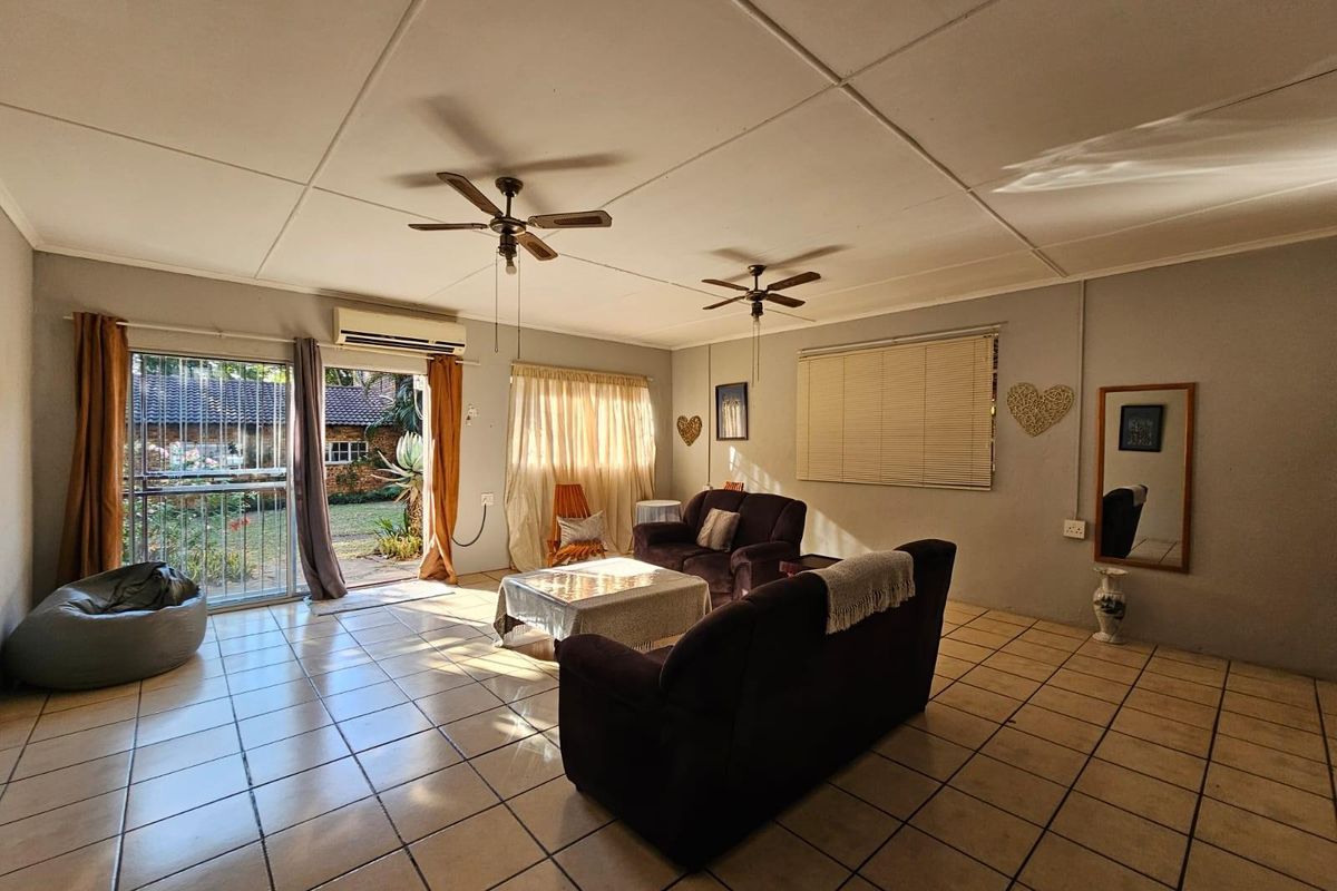 Spacious living room featuring tiled flooring, dual ceiling fans, and direct access to the rear garden through a sliding glass door.