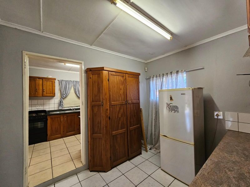A functional scullery area featuring tiled flooring and direct access to the main kitchen, offering additional storage and utility space.