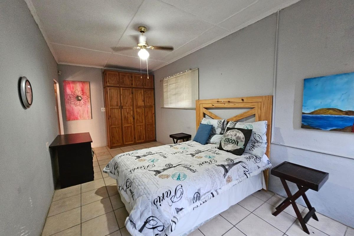 A functional bedroom featuring tiled flooring, a built-in wooden wardrobe, and a ceiling fan, offering a neutral base for potential interior updates.