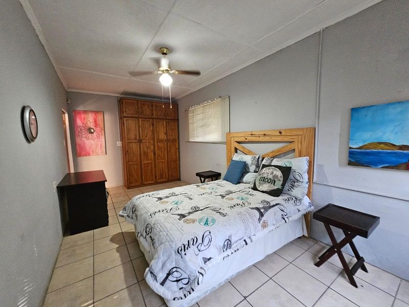 A functional bedroom featuring tiled flooring, a built-in wooden wardrobe, and a ceiling fan, offering a neutral base for potential interior updates.