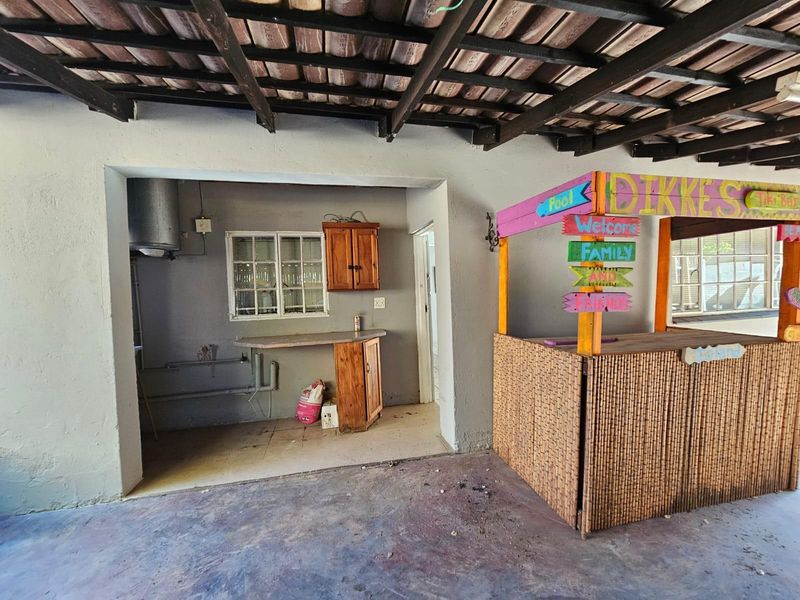 Covered outdoor patio area featuring exposed timber beams, concrete flooring, and a built-in utility or prep area with cabinetry.
