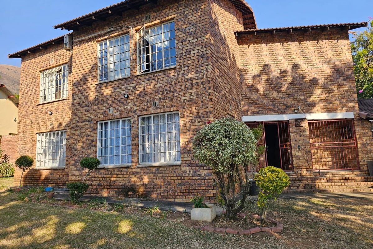 A two-story face-brick residential building featuring a tiled roof, security-barred windows, and a rear garden area.