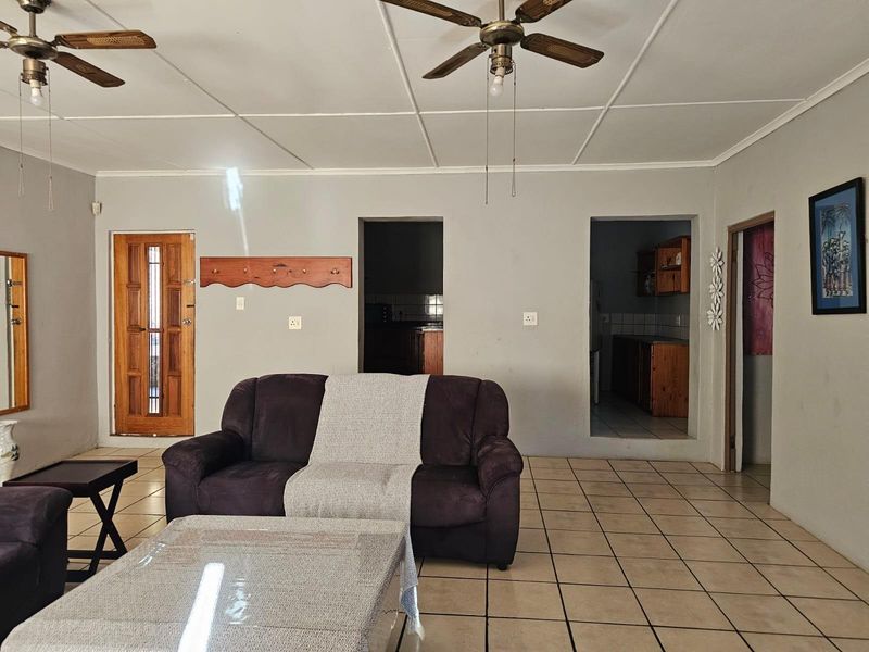 A living room featuring tiled flooring, ceiling fans, and direct access to the kitchen area through open archways.