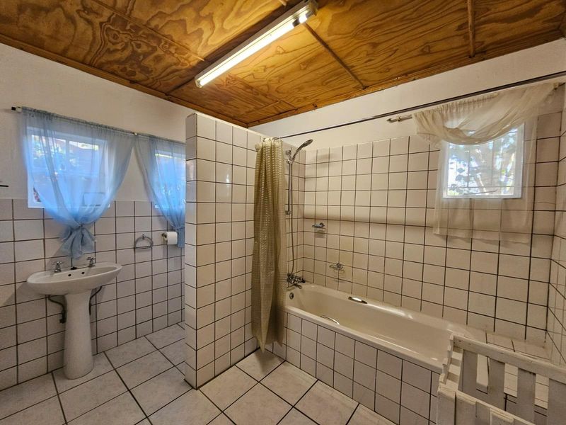 A functional bathroom featuring a pedestal basin, tiled shower-over-bath combination, and a distinctive exposed timber ceiling.