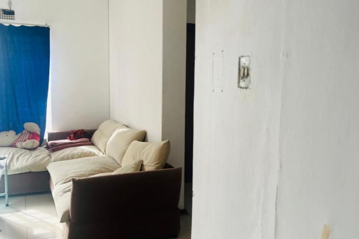 A living room area featuring tiled flooring and cornice detailing, currently showing signs of wear including wall cracks and paint deterioration.