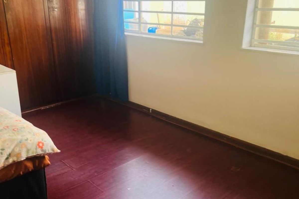 A bedroom featuring dark laminate flooring, built-in wooden wardrobes, and windows fitted with security bars.