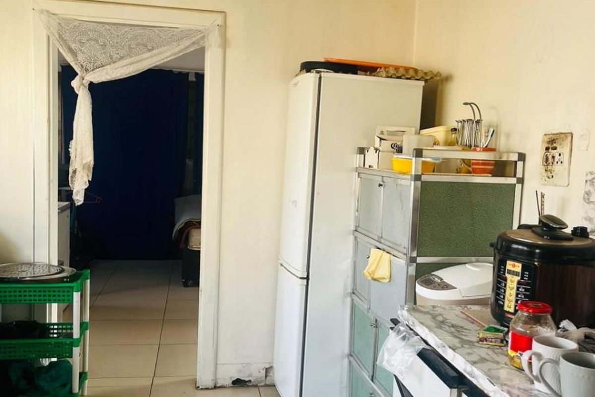 A functional kitchen area featuring tiled flooring and direct access to an adjacent room, showing signs of wear and requiring cosmetic updates.