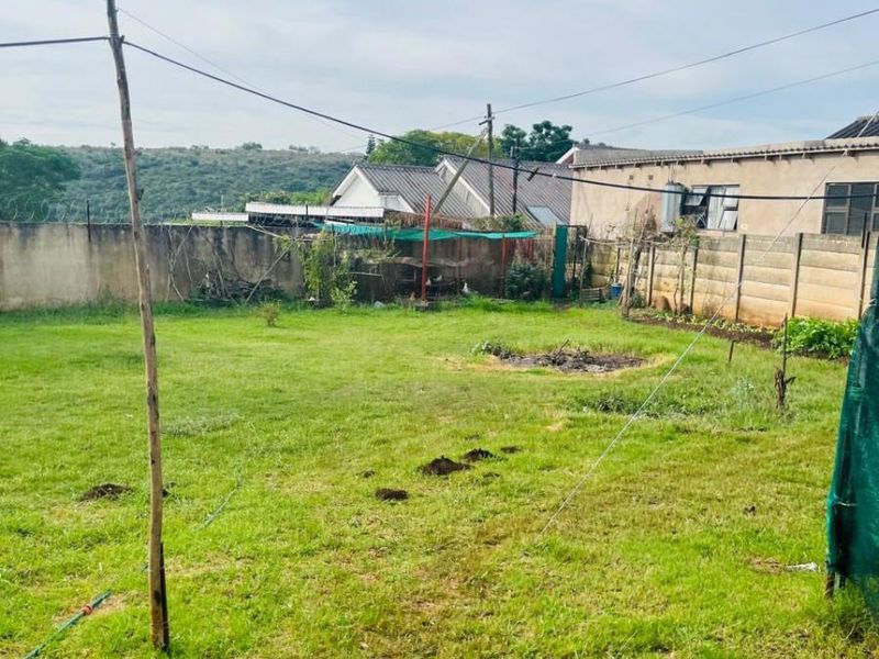 A spacious backyard garden featuring a lawn, perimeter wall with security fencing, and distant landscape views.