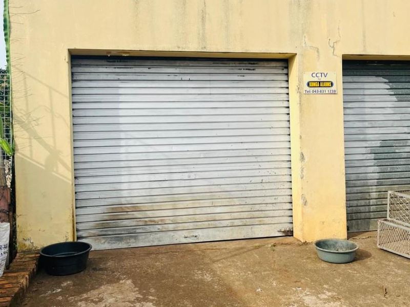 Exterior view of a garage featuring roller shutter doors and a concrete driveway, showing signs of weathering and surface staining.