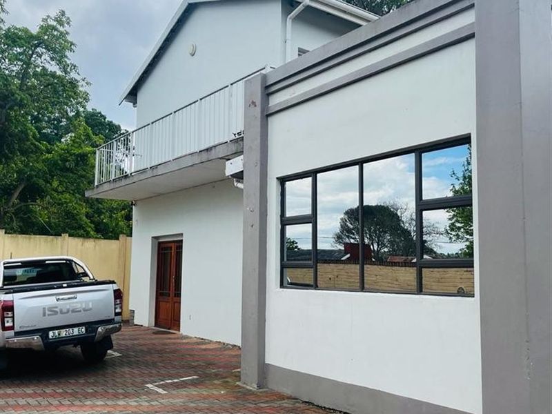 Front exterior view of the lodge featuring a paved driveway, a balcony with metal railings, and modern aluminium window frames.