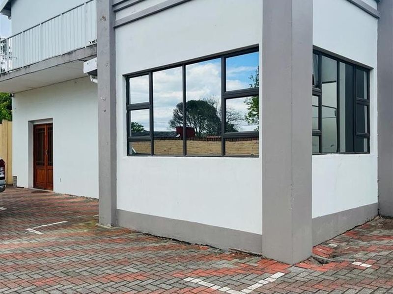 Exterior view of the lodge building featuring a paved driveway, modern aluminium window frames, and an upper-level balcony with railing.