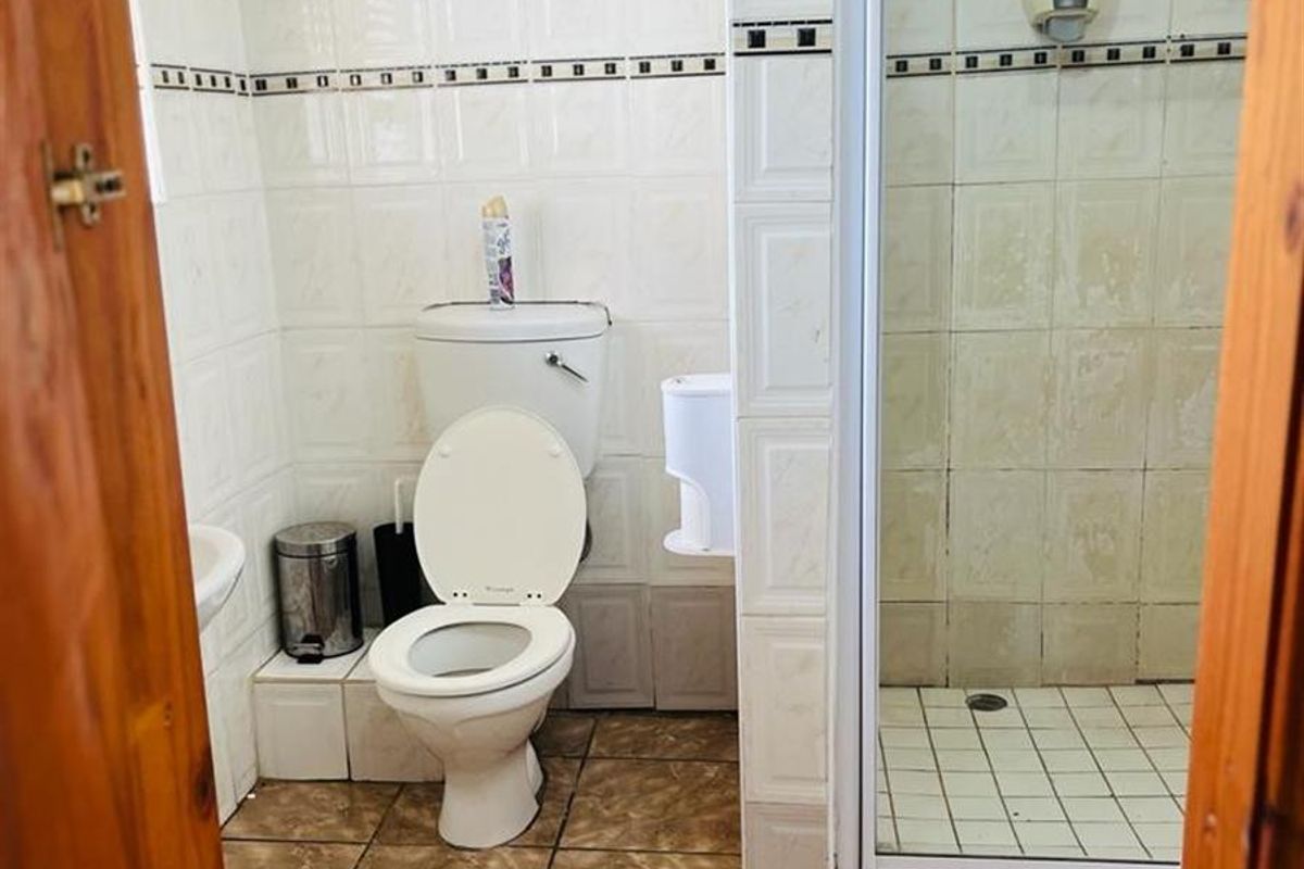 A functional bathroom featuring a shower enclosure, toilet, and wash basin with tiled walls and flooring, requiring cosmetic updates to improve its overall condition.